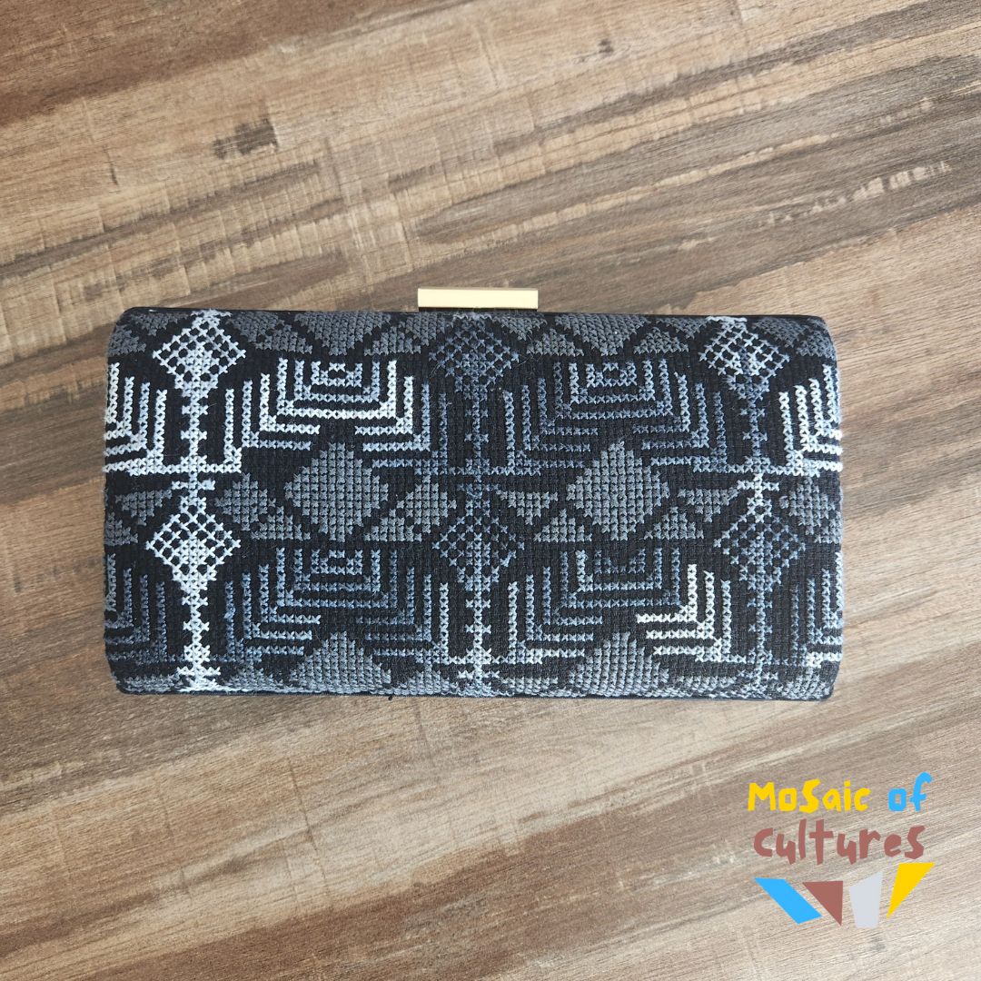 Black and white patterned clutch bag on a wooden surface with 'Mosaic of Cultures' branding.